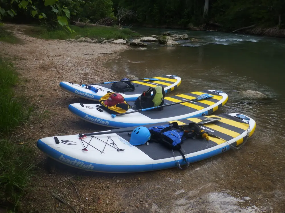 3 badfish paddle boards lying next to a river