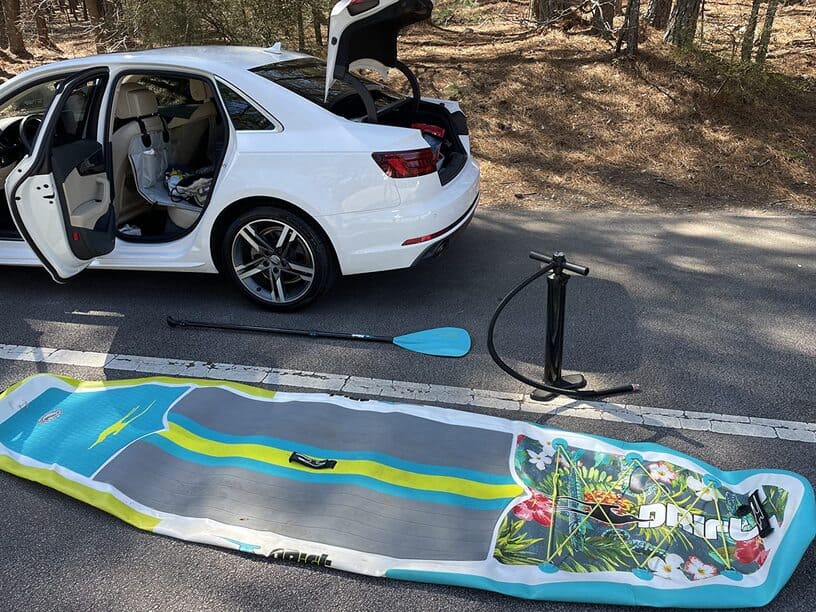 drift paddle board deflated on the ground next to a white car.